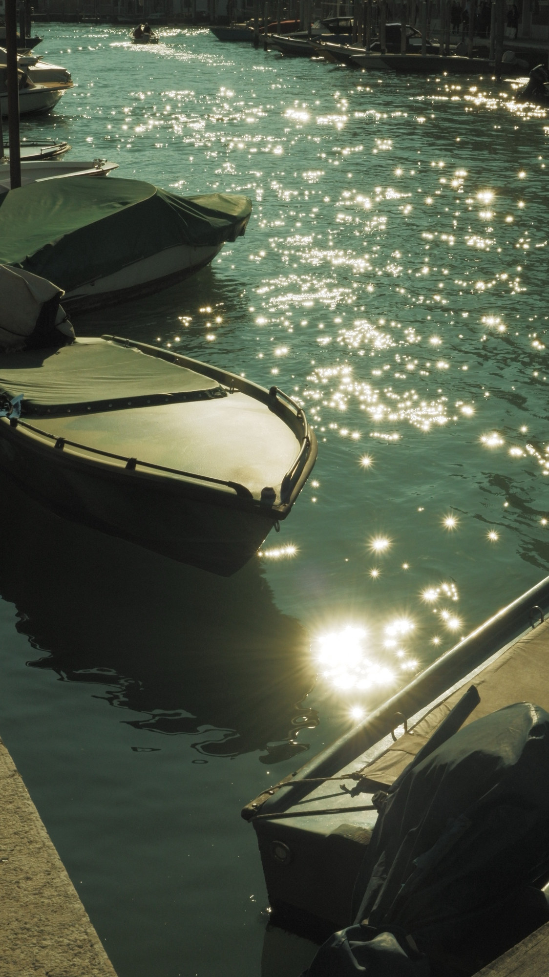 Covered boats moored on water full of sun glints