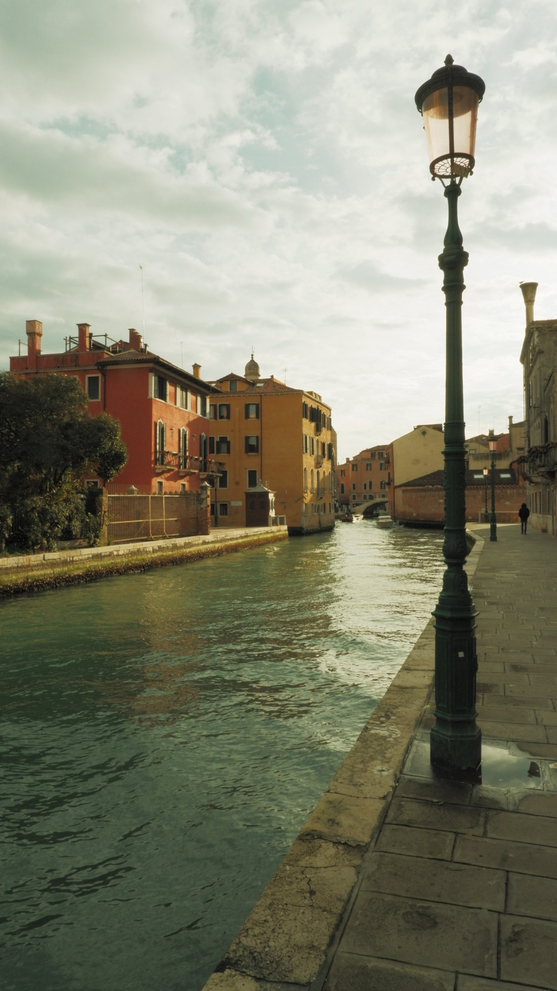 A green lamp post along a wide canal under clouds