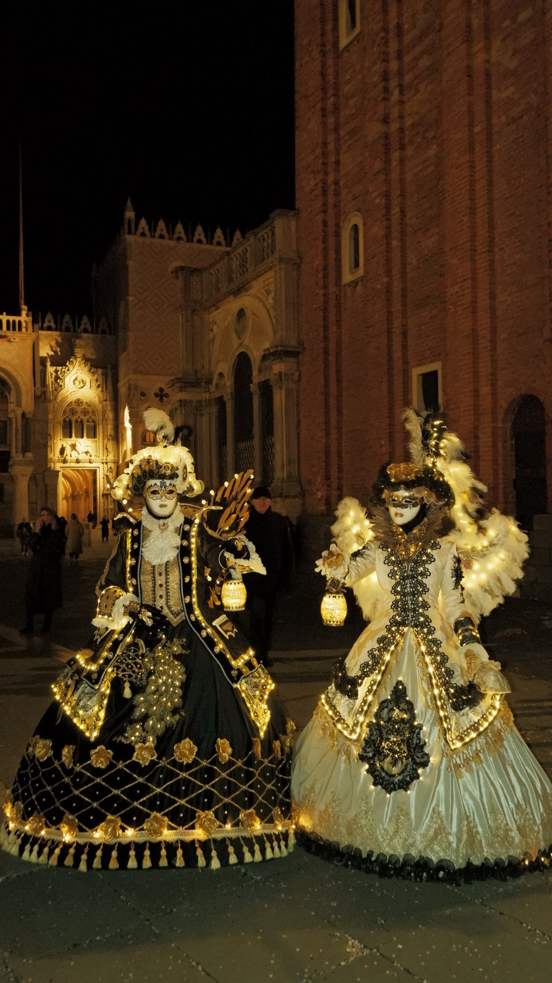 Two masked figures in illuminated gowns holding lanterns at night