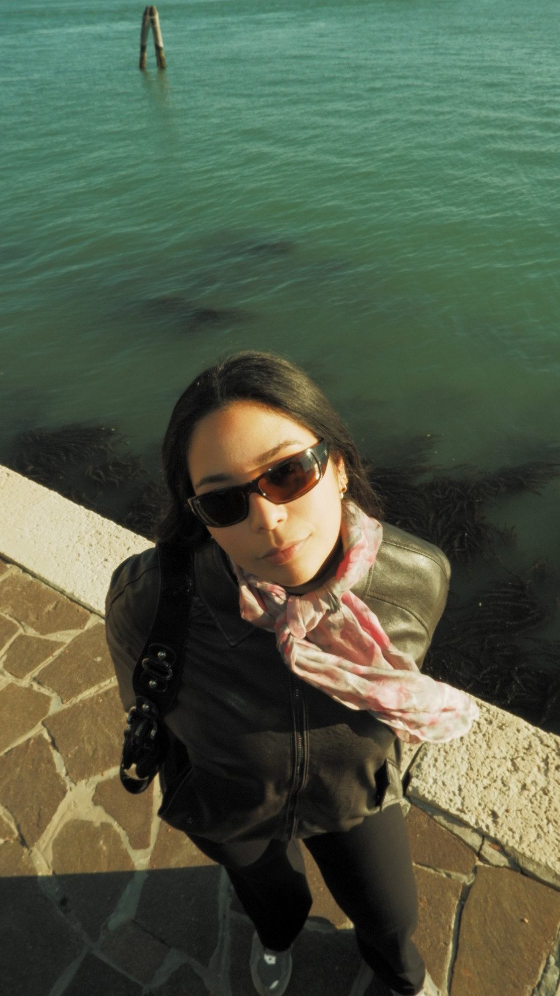 A woman in sunglasses and a pink scarf, shot from above by the water