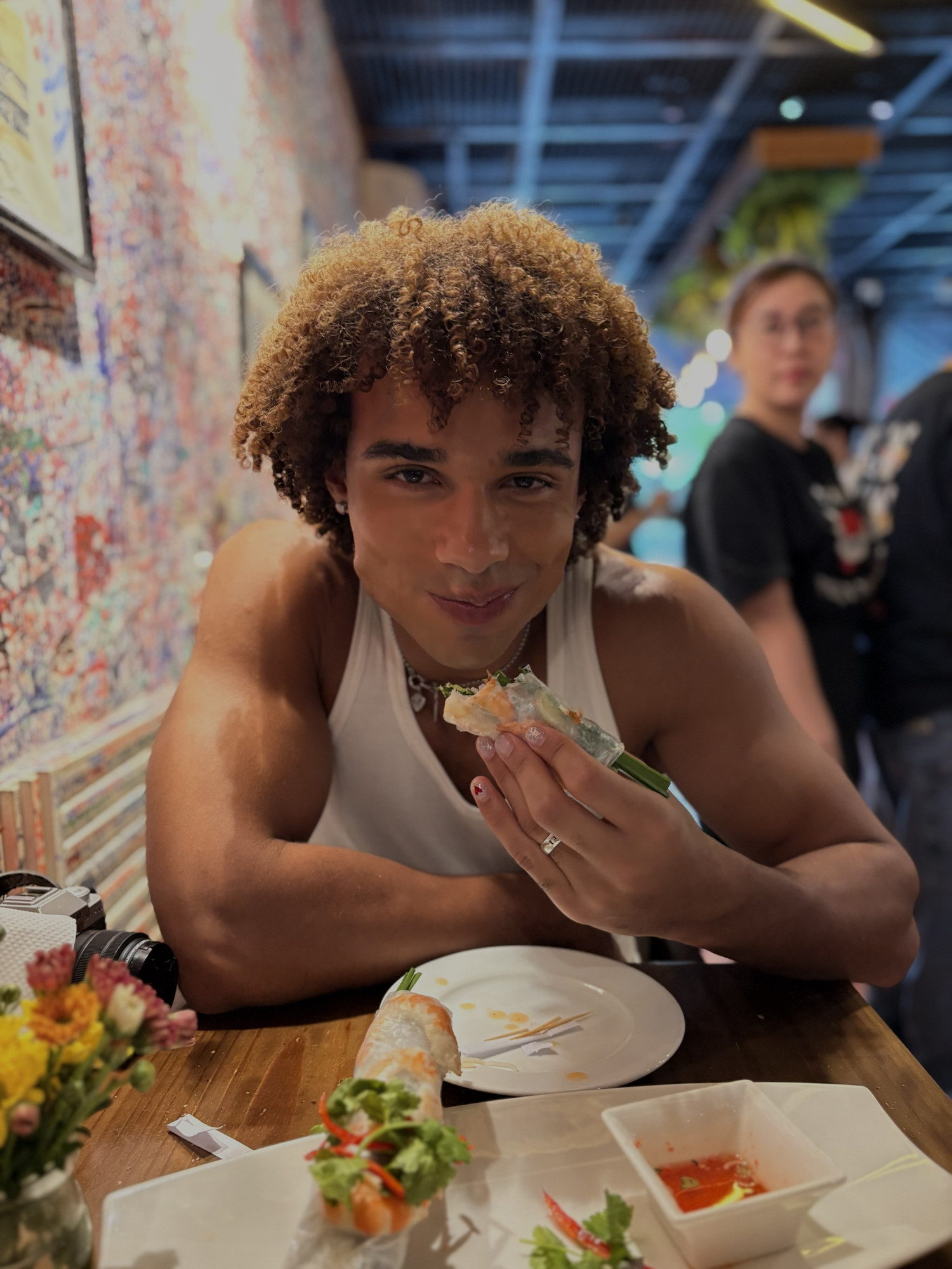 João grinning while eating a fresh spring roll at a restaurant
